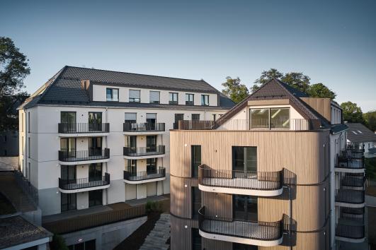 Wohnanlage mit zwei Baukörpern, einer mit Holzfassade und geschwungenen Balkonen, der andere mit heller Putzfassade