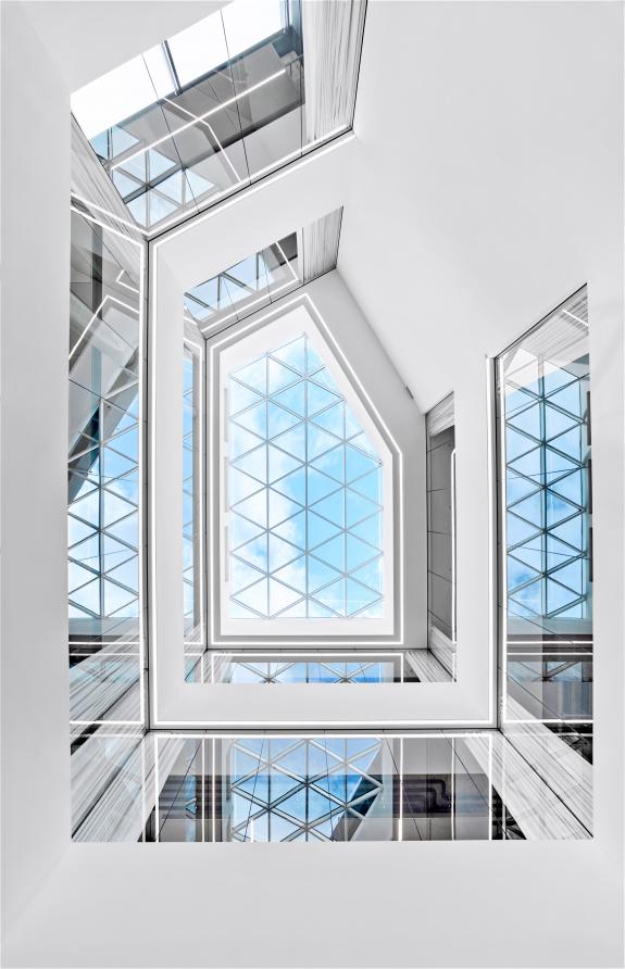 Das zentrale Atrium des HF Mixing Neubaus inszeniert Tageslicht über ein geometrisch strukturiertes Glasdach und schafft Transparenz zwischen den Ebenen – entworfen und realisiert von arcplus.