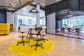 Informeller Workshop- und Kommunikationsbereich im HF Mixing Neubau mit Stehtisch, gelbem Teppich und flexibel abtrennbarem Konferenzraum – geplant und umgesetzt von arcplus.