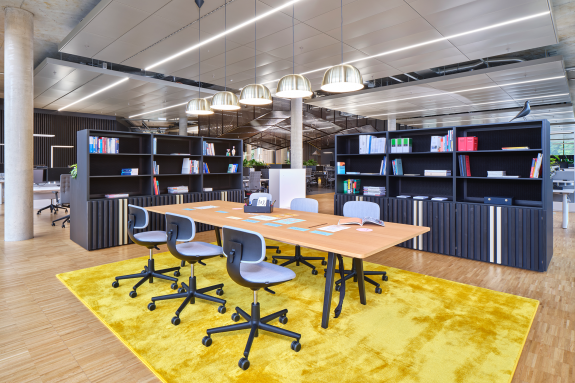 Offene Projekt- und Kommunikationsfläche mit Besprechungstisch, Bibliotheksregalen und flexibel nutzbaren Arbeitsbereichen im Verwaltungsneubau der HF Mixing Group am Unternehmensstandort in Freudenberg (Nordrhein-Westfalen). Das offene Raumkonzept fördert den Wissensaustausch, die bereichsübergreifende Zusammenarbeit und eine moderne Arbeitskultur für einen weltweit führenden Hersteller von Mischanlagen und Prozesslösungen für die Reifenindustrie, die technische Gummiwarenindustrie sowie Spezialanwendungen der Elastomerverarbeitung. Bauherr: HF Mixing Group. Geplant und umgesetzt von arc+ GmbH Freudenstadt.