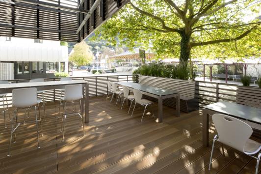 Außenterrasse des Betriebsrestaurants Chez Hans in Schiltach mit Holzboden, Tischen und Stühlen unter einem großen Baum geplant Freudenstadt