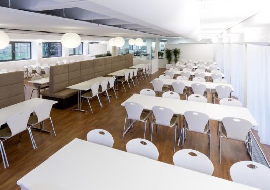 Heller Speisesaal im Betriebsrestaurant Chez Hans von Hansgrohe in Schiltach mit weißen Tischen und Stühlen, Holzboden und gepolsterten Sitznischen geplant arc+ Freudenstadt