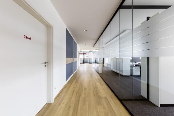 Moderner Büroflur mit raumhohen Glastrennwänden, transparenten Arbeitsbereichen und hochwertiger Innenarchitektur – geplant und umgesetzt von arc+ Freudenstadt.