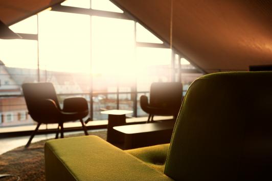 Atmosphärischer Moment im Open-Office-Bereich des ›Büro am Stadtbahnhof‹ mit loungiger Möblierung, warmem Tageslicht und Blick nach außen als Teil des New-Work-Konzepts, geplant und realisiert von arc+ Architekten