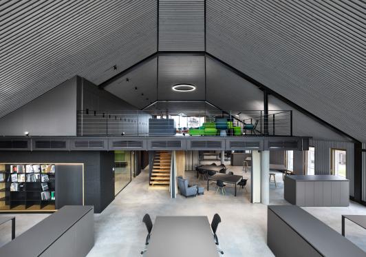 Innenansicht des Bürogebäudes ›Büro am Stadtbahnhof‹ mit offener Galerieebene, zentraler Treppe und flexibel nutzbaren Arbeits- und Aufenthaltsbereichen, geplant und realisiert von arcplus Architekten als eigenes Büro in Freudenstadt